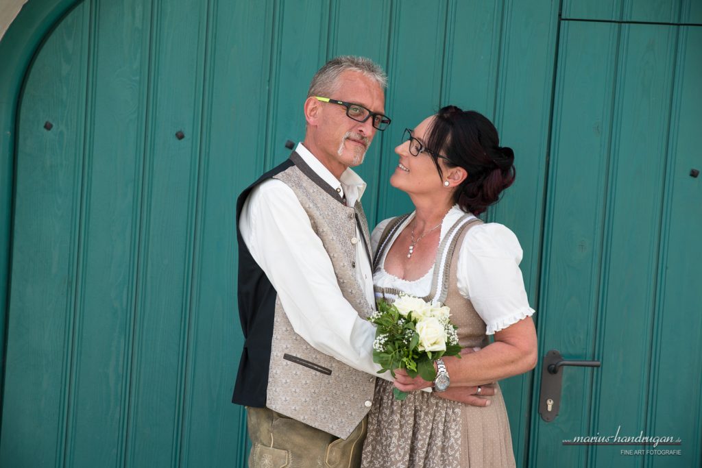 Brautpaar in Tracht mit Brautstrauß vor Holztor